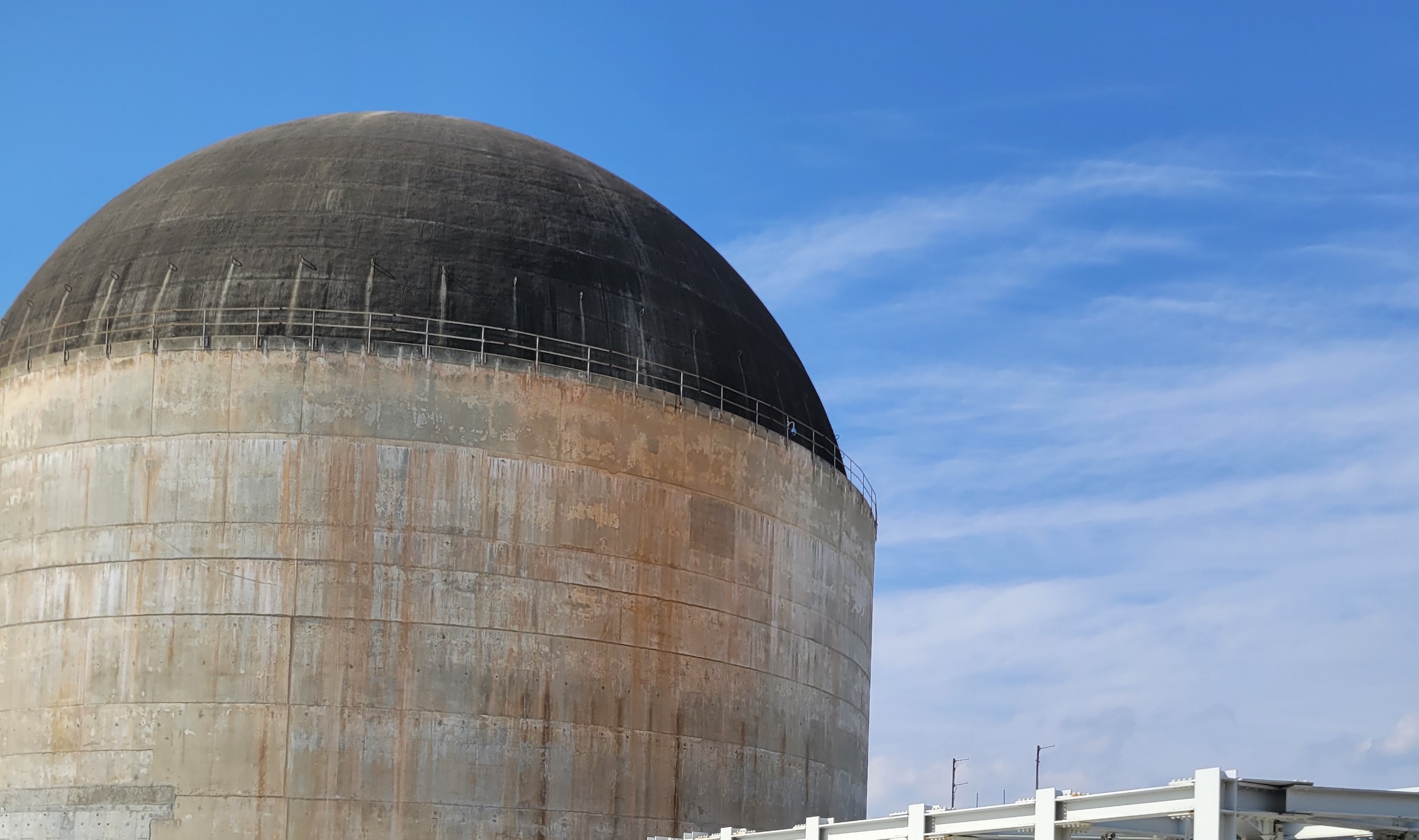 The concrete containment building of Shearon Harris Unit 1, a domed cylinder streaked with rust, under a clear blue sky.